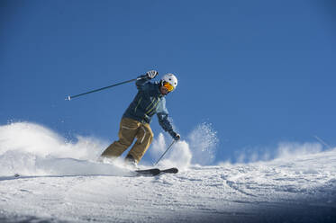 Junger Mann beim Skifahren auf Schnee vor blauem, klarem Himmel - DAMF00696