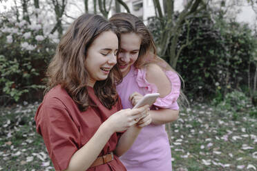 Lächelnde Teenager-Freundinnen, die im öffentlichen Park auf ihr Handy schauen - OGF00876