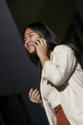Smiling young woman talking on smart phone during sunny day - VEGF03780