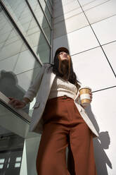 Young woman with reusable cup standing by wall during sunny day - VEGF03797