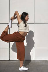 Young woman practicing Natarajasana against wall - VEGF03817