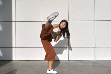 Young woman practicing kickboxing against wall - VEGF03818