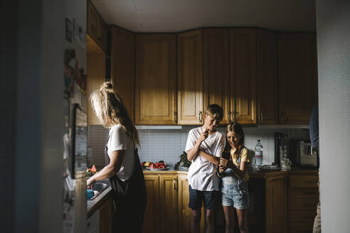 Geschwisterkind benutzt sein Smartphone, während die Mutter in der Küche Hausarbeiten erledigt - MASF21506
