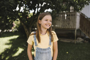 Smiling girl looking away while standing in back yard - MASF21550