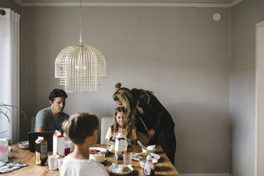 Mother kissing daughter over dining table at home - MASF21551