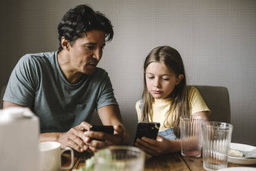 Tochter und Vater benutzen ein Smartphone über dem Esstisch zu Hause - MASF21567