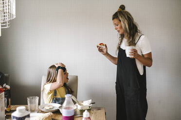 Tochter weigert sich zu frühstücken, während die Mutter zu Hause mit einer Kaffeetasse dasteht - MASF21568