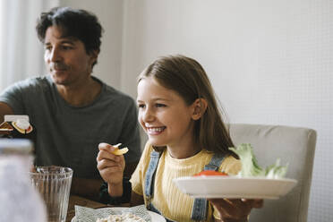 Daughter eating breakfast sitting by father at home - MASF21572