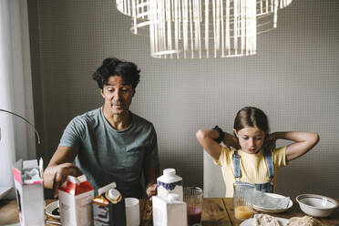 Father sitting with daughter while having breakfast at home - MASF21574