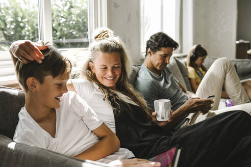 Smiling son with digital tablet sitting by mother in living room - MASF21582