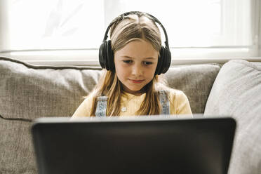Vorpubertäres Mädchen konzentriert sich beim E-Learning am Laptop im Wohnzimmer - MASF21583