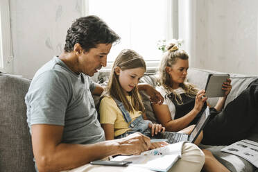 Father teaching daughter while mother sitting beside using digital tablet at home - MASF21590