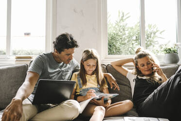 Daughter doing homework sitting by mother and father in living room - MASF21591