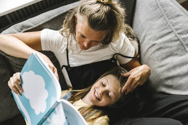 Tochter liest mit Mutter im Wohnzimmer ein Buch - MASF21593