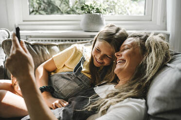 Smiling mother and daughter using digital tablet in living room - MASF21602