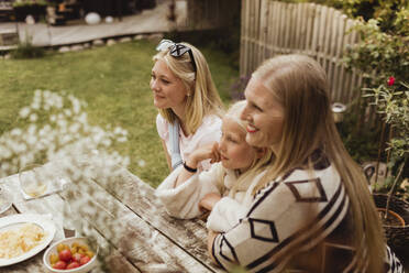 Smiling mother and daughters sitting in back yard - MASF21616