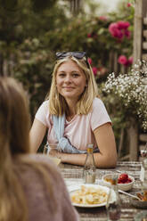 Smiling teenage girl sitting with food at table during dinner party - MASF21620