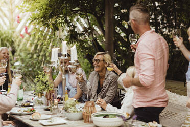 Fröhliche Familie stößt mit Weingläsern bei einem Abendessen im Vorgarten an - MASF21635