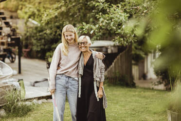 Lächelnde Enkelin mit Arm um Großmutter im Hinterhof stehend - MASF21648