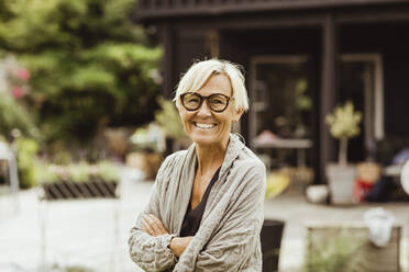 Smiling mature woman with arms crossed in back yard - MASF21652