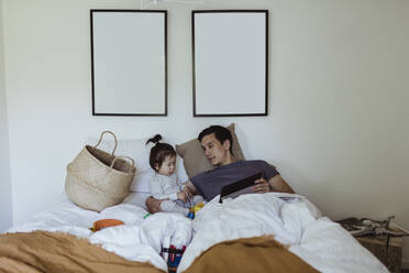 Vater mit männlichem Kleinkind hält digitales Tablet im Schlafzimmer zu Hause - MASF21663