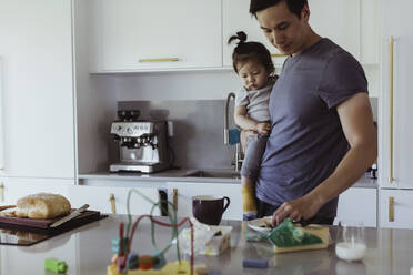 Father with food carrying male toddler by kitchen counter - MASF21682