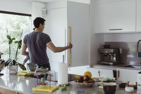 Vater öffnet Kühlschrank, während er seinen kleinen Sohn in der Küche trägt - MASF21684