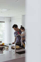 Vater trägt männliches Kleinkind bei der Zubereitung von Essen in der Küche - MASF21685