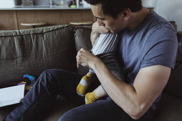 Father checking son's diaper while sitting on sofa in living room - MASF21696