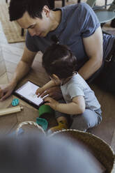 Vater benutzt digitales Tablet und sitzt mit seinem kleinen Sohn zu Hause - MASF21697