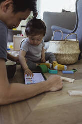 Baby-Sohn schaut in digitale Tablet sitzen mit Vater im Wohnzimmer - MASF21698