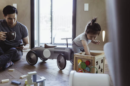 Männliches Kleinkind spielt mit Puzzle-Spielzeug, während der Vater sein Smartphone im Wohnzimmer benutzt - MASF21703