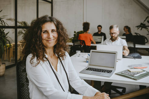 Porträt einer lächelnden Geschäftsfrau, die in einem Coworking-Büro am Laptop sitzt - MASF21706