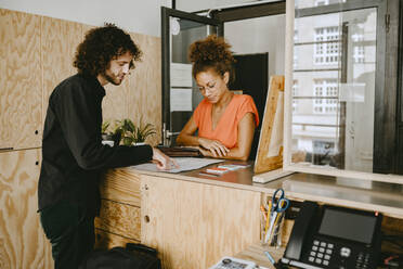 Male entrepreneur discussing with female colleague over document at coworking office - MASF21720