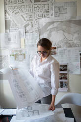 Young female architect working with blueprints - CAVF92141