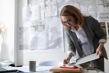 Serious businesswoman with clipboard reading notes on smartphone - CAVF92145