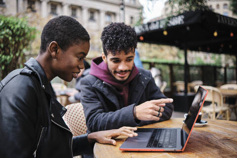 Mann zeigt auf Laptop, während er mit einem Freund in einem Straßencafé sitzt, lizenzfreies Stockfoto