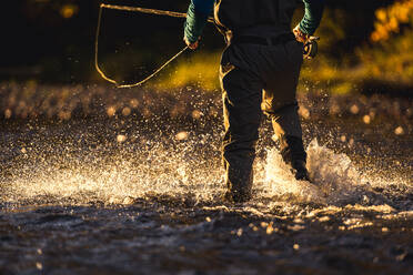 Fly-fisherman wading through river in late evening light - CAVF92214