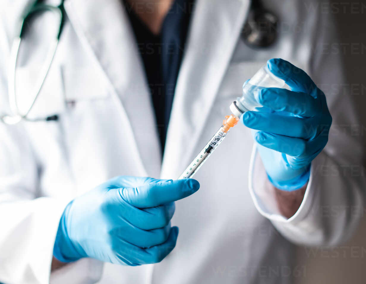 Arzt im weißen Kittel zieht Impfstoff in eine Spritze zur Injektion.,  lizenzfreies Stockfoto