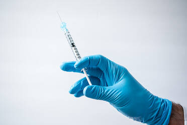 Hand in Handschuh hält eine Spritze mit einem Impfstoff auf weißem Hintergrund. - CAVF92225
