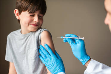 Nervös aussehendes Kind, das von einem Arzt geimpft wird, der eine Nadel hält. - CAVF92226