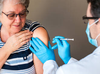 Ältere Frau, der ein Arzt einen Impfstoff in den Oberarm spritzt. - CAVF92229