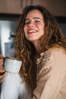 Young female drinking hot beverage and smiling to camera - CAVF92250
