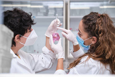 Two young female scientists wearing face masks using a flask. Laboratory research concept. - CAVF92253