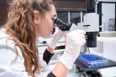 Young female scientist looking through a microscope in a laboratory. Laboratory research concept. - CAVF92259