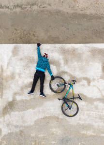 Rückansicht eines Mannes, der an einer Betonwand hängt und ein Rad hält - CAVF92274