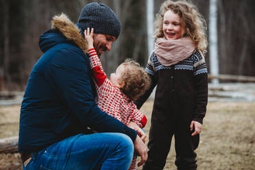Vater lächelt und umarmt Kinder im Wald im Winter in Norwegen - CAVF92307