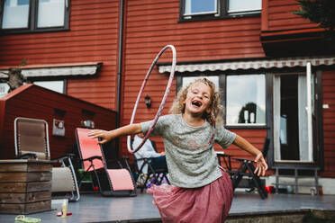 Nettes Mädchen hat Spaß mit Hula-Hoop-Reifen im Hinterhof mit roten Holzhaus - CAVF92310