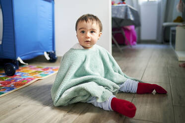 Cute baby girl playing with towel while sitting on floor at home - KIJF03548