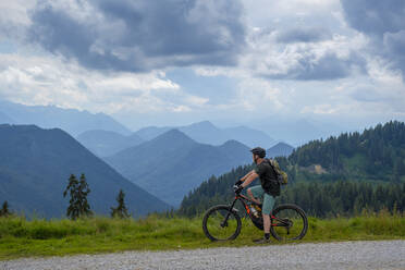 Entdecker, der die Aussicht betrachtet, während er mit seinem Mountainbike am Weg bei Roßstein und Buchstein steht, Bayern, Deutschland - LBF03336
